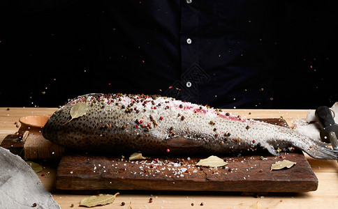 木板上的无头鲑鱼片洒满大白盐和胡椒食用鱼的加工过程背景图片