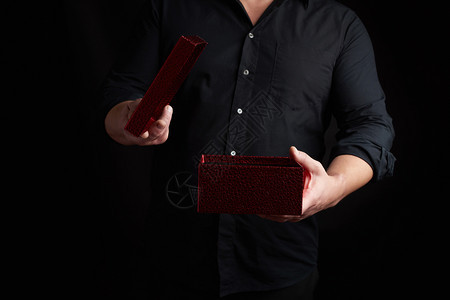 穿黑衬衫的成人男子拿着一个亮的红纸箱惊喜和节日问候的概念图片