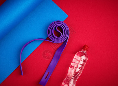 二对塑料哑铃紫弹橡胶和瓶装水放在红色新胎垫顶视培训设备上图片