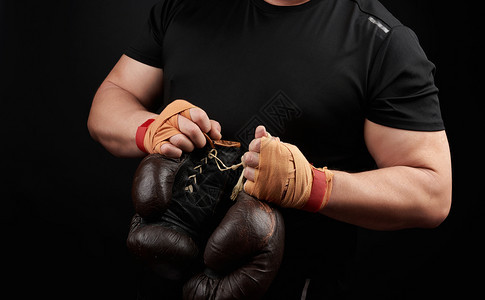 身穿黑色制服的肌肉运动员手上握着非常古老的棕色拳击手套双被绑上橙色弹运动绷带黑色背景复制空间图片