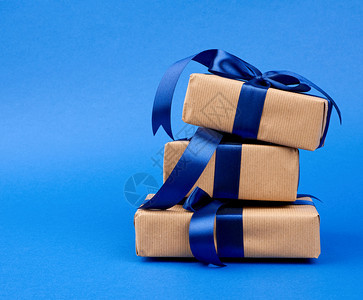 裹在棕色克拉夫纸上的矩形盒绑在丝蓝带上礼物在深蓝色背景上图片