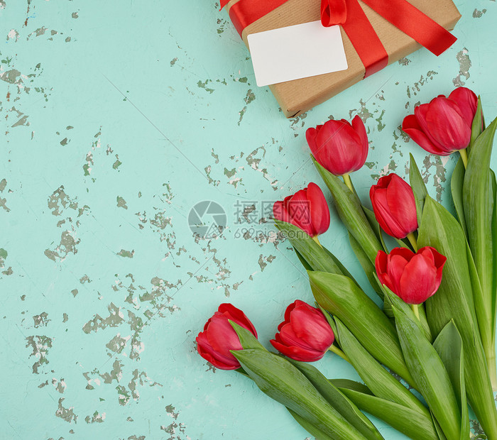 红色盛开的郁金香花束有绿色叶子包着的礼物在绿色背景的棕手工艺纸上复制空间生日情人节的喜庆背景图片