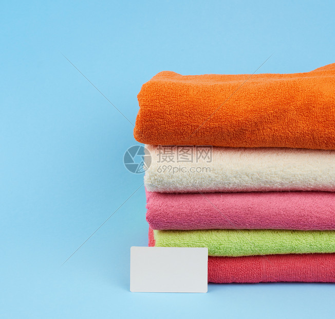 淋浴后擦的多色毛巾堆叠和蓝背景的白纸名片图片