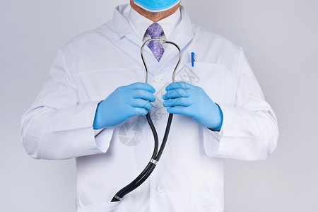 身穿白大衣和领带的医生手上握着黑色听话望远镜戴蓝手套白底医学研究图片