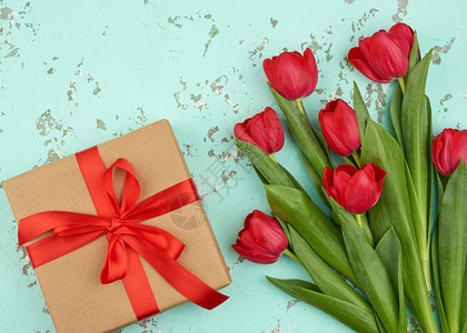 红色盛开的郁金香花束配有绿色叶子棕手工艺纸包着的礼物以及绿色背景顶层观点的丝绸红色带生日情人节的喜庆背景图片