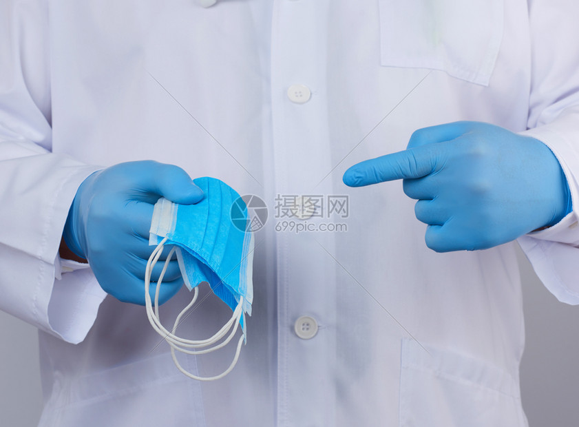 穿白色大衣的医生蓝色乳胶消毒手套将防病和细菌的护从属剂和细菌的剂的护服放在他手上紧闭图片