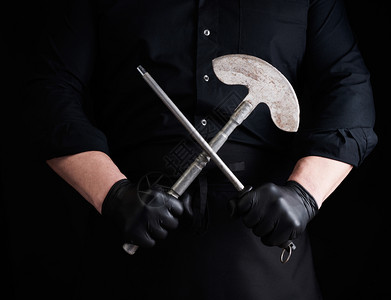 穿黑色制服和乳胶手套的男黑衣和乳胶手套的男厨师持有用于肉类和蔬菜的一把大刀和用于黑底的一把金属磨和用于黑底的一把金属磨图片