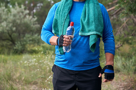 成年运动员正站在大自然中间穿着蓝色制服用绿毛巾一边用透明塑料水瓶图片