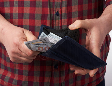 身穿格斗红衬衫的男人拿着一个钱包满百美元纸币钞票工资概念财富图片