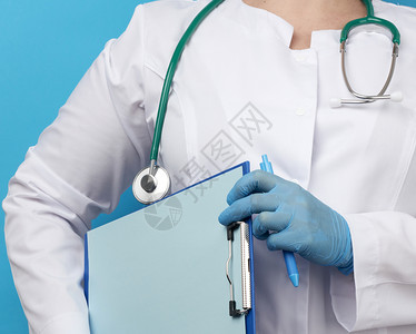 穿白大衣的女医务人员蓝色的乳胶手套拿着平板剪片纸蓝色背景关闭图片