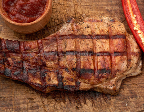 肋骨上的猪肉炸牛排躺在古老的棕褐木板上旁边是新鲜红辣椒图片