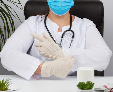 白制服一次医疗面具的女生坐在桌子的椅上将白无菌乳胶手套放在他的上医生办公室图片