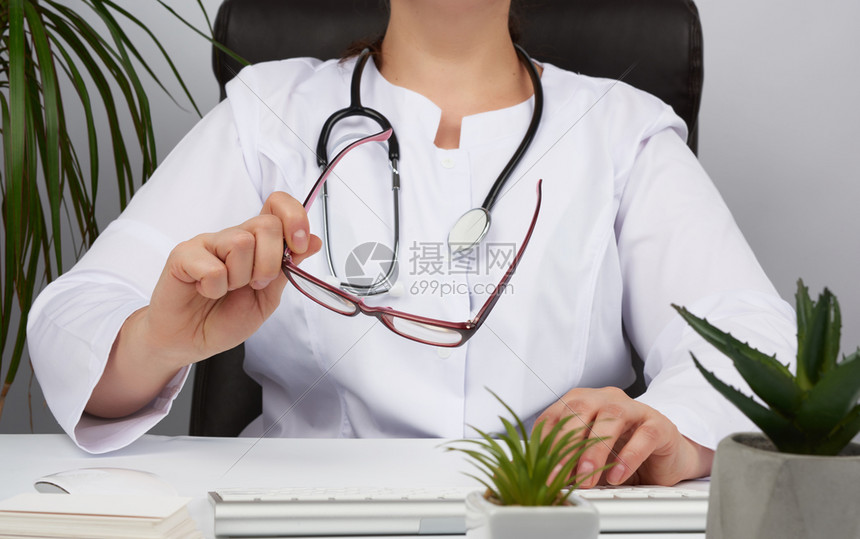穿着白色制服一次医疗面罩的女生坐在桌子的椅上工作手里握着眼镜办公室图片