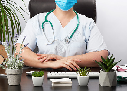 医生手套坐在办公室的白工作桌旁病人在诊所接受双手放在胸前突出姿势图片
