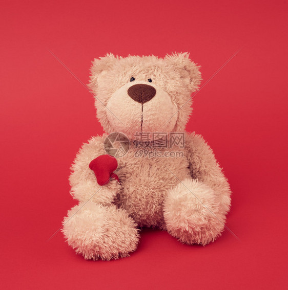 小棕色泰迪熊玩具坐在红色背景关闭图片