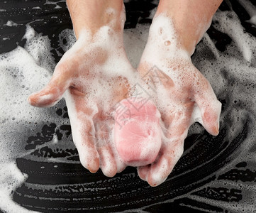 用粉色肥皂洗手过程用黑色背景顶视卫生概念的白泡沫洗手身体部分图片