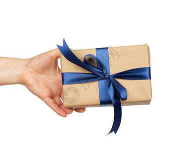 用棕色手纸包着的礼物上面有捆绑的丝蓝弓主题在白色背景惊喜概念和节日礼物上被孤立图片