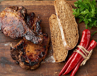 厨房切菜板上骨头的烤猪肉牛排切片黑麦面粉包和红辣椒顶视图片