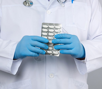 医生治疗师穿着白色制服的外套蓝色消毒手站立用白色底的泡包装一堆药丸图片