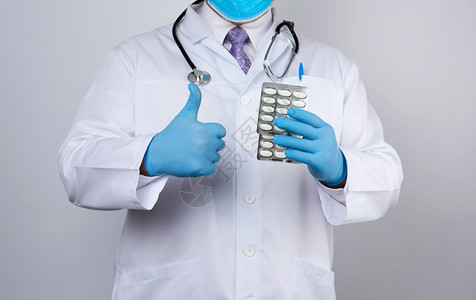 医生治疗师穿着白色制服的外套蓝色消毒手站立用白色底的泡包装一堆药丸图片