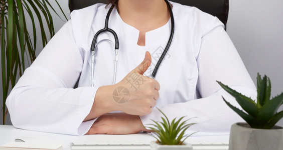 身穿白大衣的女医务人员展示手持势批准概念治疗师坐在办公桌的椅子上图片