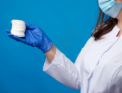 穿白色大衣的医生蓝色乳胶医疗手套内装一堆蓝色背景的棉花化妆盘图片