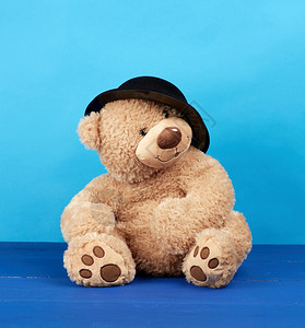 蓝色背景的黑帽子大棕色泰迪熊图片