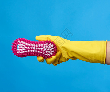 用黄色橡皮手套打扫房屋将粉红色塑料刷放在蓝背景上图片