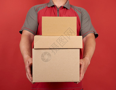 穿T恤衫的成年男子拿着一大堆纸板棕色盒子红背景货物交付的概念移动图片