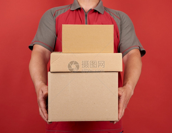 穿T恤衫的成年男子拿着一大堆纸板棕色盒子红背景货物交付的概念移动图片