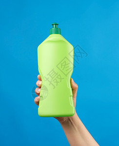 手里拿着绿色塑料瓶有洗涤剂用于碗和家里的东西蓝底物品图片