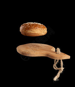 烤圆包含芝麻种子在棕色木切板黑背景汉堡成分上盘旋图片