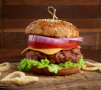 芝士汉堡加西红柿洋葱烧烤小菜和芝麻面包放在旧木制剪板上棕色背景快餐图片