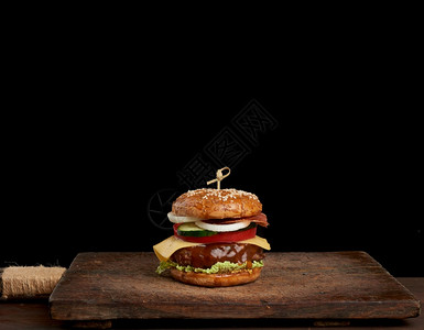 芝士汉堡加番茄洋葱烧烤小菜和芝麻面包放在一个旧木制剪板上黑色背景快餐复制空间背景图片