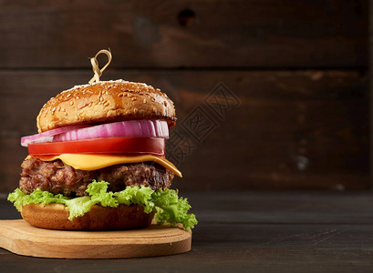 芝士汉堡加番茄洋葱烧烤小菜和芝麻面包放在一个旧木切面板上棕色背景快餐复制空间图片