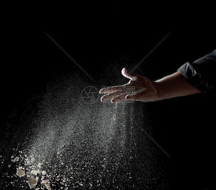 面包师的手把一些白面粉扔在黑色背景上粒子向不同方飞去图片