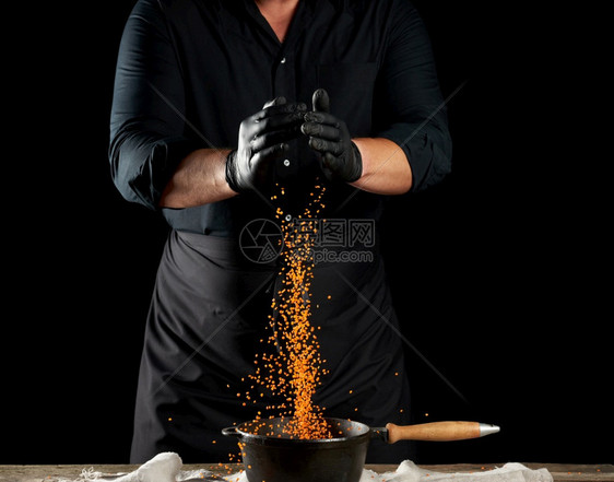 黑衣服主厨和乳胶手套将生扁豆倒入圆制铁锅手柄黑色背景图片