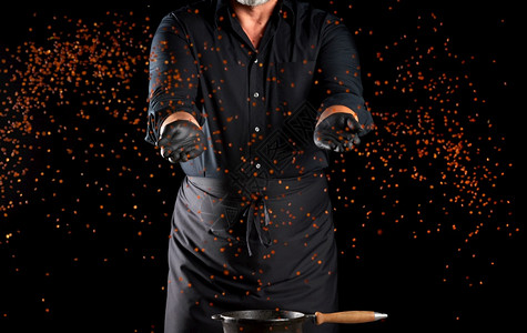 身穿黑色制服厨师的将扁豆颗粒扔在黑色背景上产品飞向不同方图片