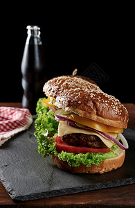 美味的汉堡配有炸牛肉切菜和洋葱番茄面粉包和芝麻种子木板上快餐瓶子后加饮料图片