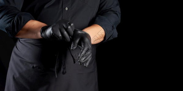 厨师穿黑色衬衫和围裙在准备食物黑色背景复制空间之前将黑色乳胶手套戴在上图片