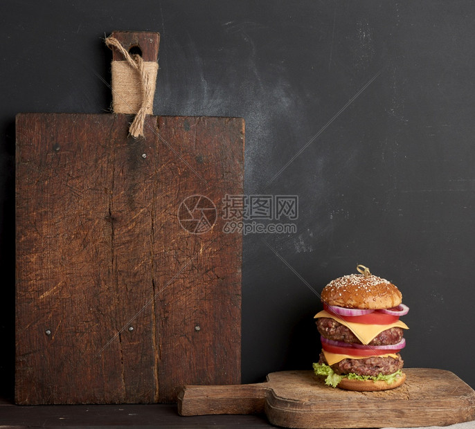 配西红柿洋葱烧烤小菜和芝麻面包的双士汉堡一个旧木制切板黑色背景登记地点图片