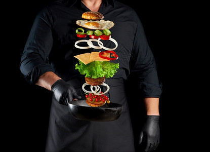 身穿黑色制服的成年男子拿着一个铁环煎锅配有上浮芝士汉堡成份麻士番茄洋葱肉饼辣椒图片