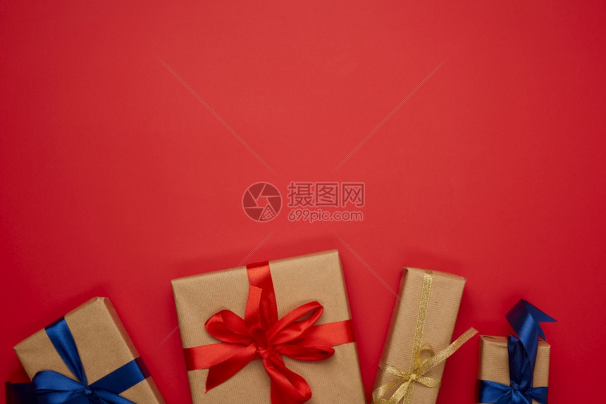 以棕纸包裹并绑上蓝色丝带弓红背景的礼物顶视图复制空间图片