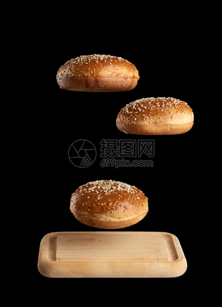 烤圆包含芝麻种子在棕色木切板黑背景汉堡成分上盘旋图片