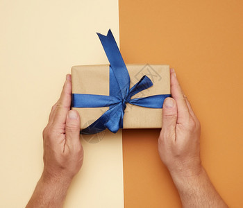 男手拿着礼物盒在棕色背景上鞠躬为假日赠送礼物的概念图片