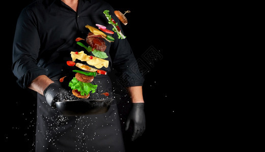 穿着黑色制服的男子拿着一个铁环煎锅配有上浮芝士汉堡成份麻奶酪番茄洋葱肉饼辣椒复制空间图片