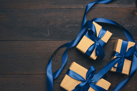 以棕色纸包成的长方形盒子绑上蓝色丝带有弓棕色木背景的礼物顶视图片
