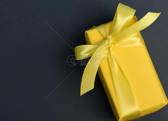 盒形矩礼品包裹在黄色纸上绑有丝黄色带顶视图黑色背景图片