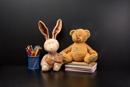 可爱的兔子和棕色泰迪熊坐在黑色粉笔板背景上回到学校图片