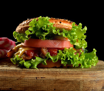 在木制棕色厨房板上加肉绿色生菜和番茄酱的芝士汉堡图片